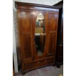 A 4' 2 1/2" Edwardian inlaid mahogany wardrobe with hanging space enclosed by a bevelled oval mirror