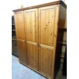 A 4' 10" modern waxed pine triple wardrobe with shelves and hanging space enclosed by panelled