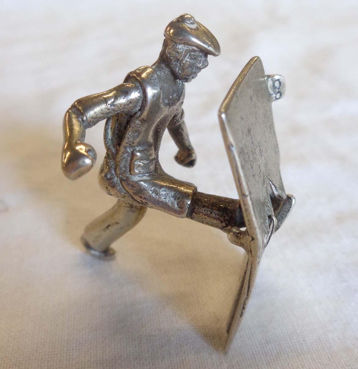 A Dutch hallmarked white metal novelty figure of a workman kicking a door in