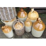 Seven assorted stoneware flagons, some branded, two with wicker basket cladding, etc.