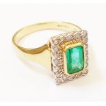 A hallmarked 750 gold panel ring, set with central emerald within a diamond encrusted border