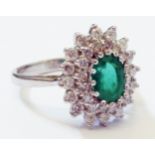 A marked 750 white metal ring, set with central oval emerald within a diamond encrusted border