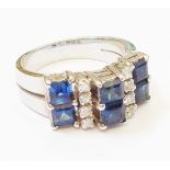 An unmarked high carat white metal ring of stepped design, set with six square cut sapphires and two