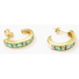 A pair of marked 14k yellow metal half hoop ear-rings, each with four channel set emeralds