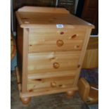 An 18" modern polished pine bedside chest of three drawers, set on turned feet