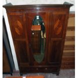 A 4' 2 1/2" Edwardian inlaid mahogany wardrobe with hanging space enclosed by a bevelled oval mirror