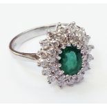 A marked 750 white metal ring, set with central oval emerald within a diamond encrusted border