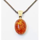 A yellow metal framed pendant with reconstituted amber cabochon on a marked 9ct. kerb-link neck