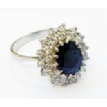 A marked 18ct. white metal ring, set with central dark blue oval sapphire within a diamond encrusted