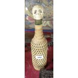 A wicker clad wine bottle with human skull shaped stopper