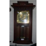 An early 20th Century stained oak cased wall clock with brass dial, visible coppered pendulum and
