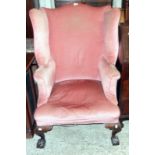 A late 19th Century wing-back armchair in the early Georgian style, upholstered in old rose coloured