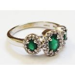 A hallmarked 585/14k white gold ring, each of the triple settings with central oval emerald within a