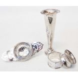 A silver tea strainer with pierced handles, two napkin rings and a silver trumpet vase with loaded