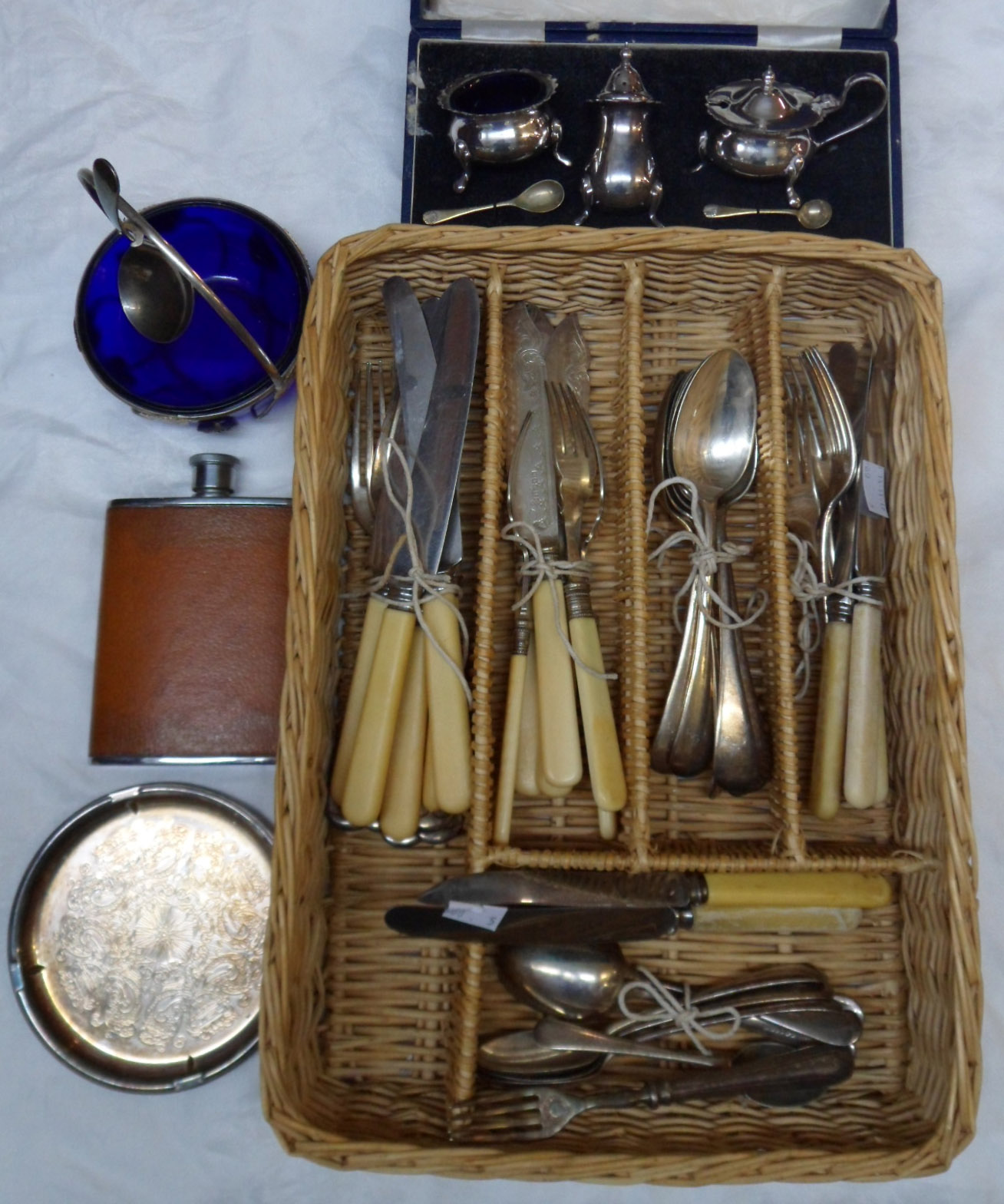 A wicker cutlery tray containing a cased silver plated three piece condiment set, plated cutlery,