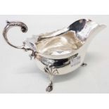 A Walker and Hall silver gravy boat in the Georgian style with cast scroll handle, set on triple