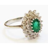 A marked 750 white metal ring, set with central oval emerald within a diamond encrusted border