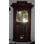 An early 20th Century stained oak cased wall clock with brass dial, visible coppered pendulum and