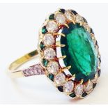 An unmarked yellow metal ring, set with 14 mm oval emerald within a sixteen stone diamond border