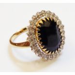 A hallmarked 375 gold ring, set with large central oval dark sapphire within a diamond encrusted