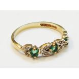 A yellow metal ring set with three small emeralds interspersed with pairs of tiny diamonds