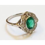 A 1920`s style high carat white metal ring, set with central oval emerald within a diamond encrusted