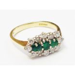 A hallmarked 750 gold ring, set with three central emeralds within a diamond encrusted border