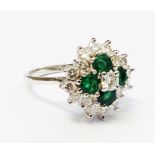 A hallmarked 18ct. white gold ring, set with four emeralds with central diamond within a diamond