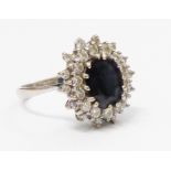 A marked 18ct. white metal ring, set with central dark blue oval sapphire within a diamond encrusted