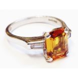 An 18ct. white gold ring, set with central emerald cut golden yellow sapphire and flanking