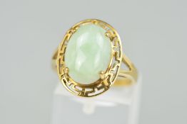 A 9CT GOLD JADE RING, the oval jade cabochon within an open Greek key surround to the bifurcated