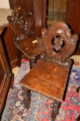 A PAIR OF EARLY 20TH CENTURY HEAVILY CARVED OAK HALL CHAIRS, the back carved with a tribal faceon