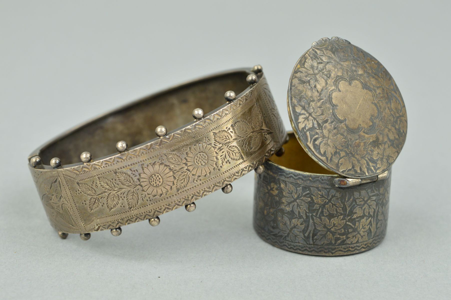 AN EARLY 20TH CENTURY SILVER BANGLE AND A LATE VICTORIAN PILL BOX, the front half bangle engraved