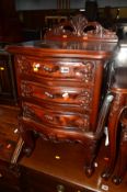 A REPRODUCTION CARVED MAHOGANY BEDSIDE CHEST OF THREE DRAWERS