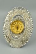 A LATE VICTORIAN EASLE BACKED SILVER MOUNTED OVAL CLOCK, repousse decorated with foliate scrolls and