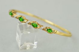 A 9CT GOLD GEM BANGLE, the hinged bangle set with four oval green gems interspaced by angled tapered