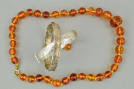 TWO SILVER HINGED BANGLES AND A MODIFIED AMBER NECKLACE, the bangles with engraved decoration to the