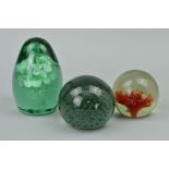 A GREEN GLASS DUMPY WEIGHT with floral vase inclusion and two other glass paperweights (3)