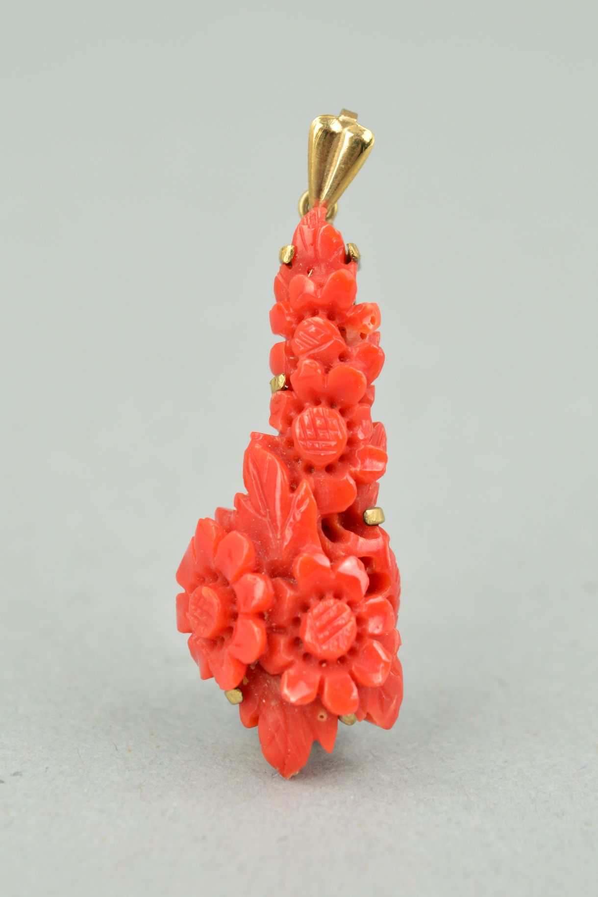 A DYED CARVED CORAL 9CT GOLD PENDANT of elongated outline, the coral carved to depict flowers and