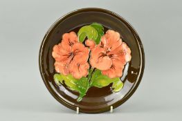 A MOORCROFT POTTERY PLATE, 'Hibiscus' pattern on brown ground, impressed marks, brown painted
