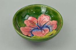 A MOORCROFT POTTERY FOOTED BOWL, 'Hibiscus' pattern on green ground, paper label to base, diameter