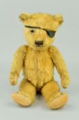 A GOLDEN PLUSH TEDDY BEAR, glass eyes (one missing), vertical stitched nose, partially shaved