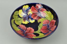 A LARGE MOORCROFT FOOTED BOWL, 'Hibiscus' pattern on dark blue ground, impressed marks and paper