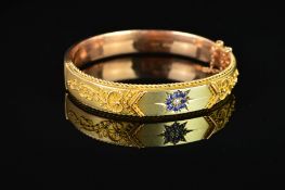AN EARLY 20TH CENTURY 9CT GOLD SAPPHIRE AND DIAMOND OVAL HINGED BANGLE, centring on a round
