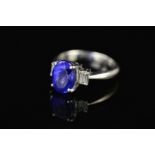 A MODERN TANZANITE AND DIAMOND THREE STONE RING, centring on an oval mixed cut tanzanite measuring