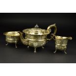 AN EDWARDIAN/GEORGE V SILVER THREE PIECE CIRCULAR TEASET, wavy rims repousse decorated with birds