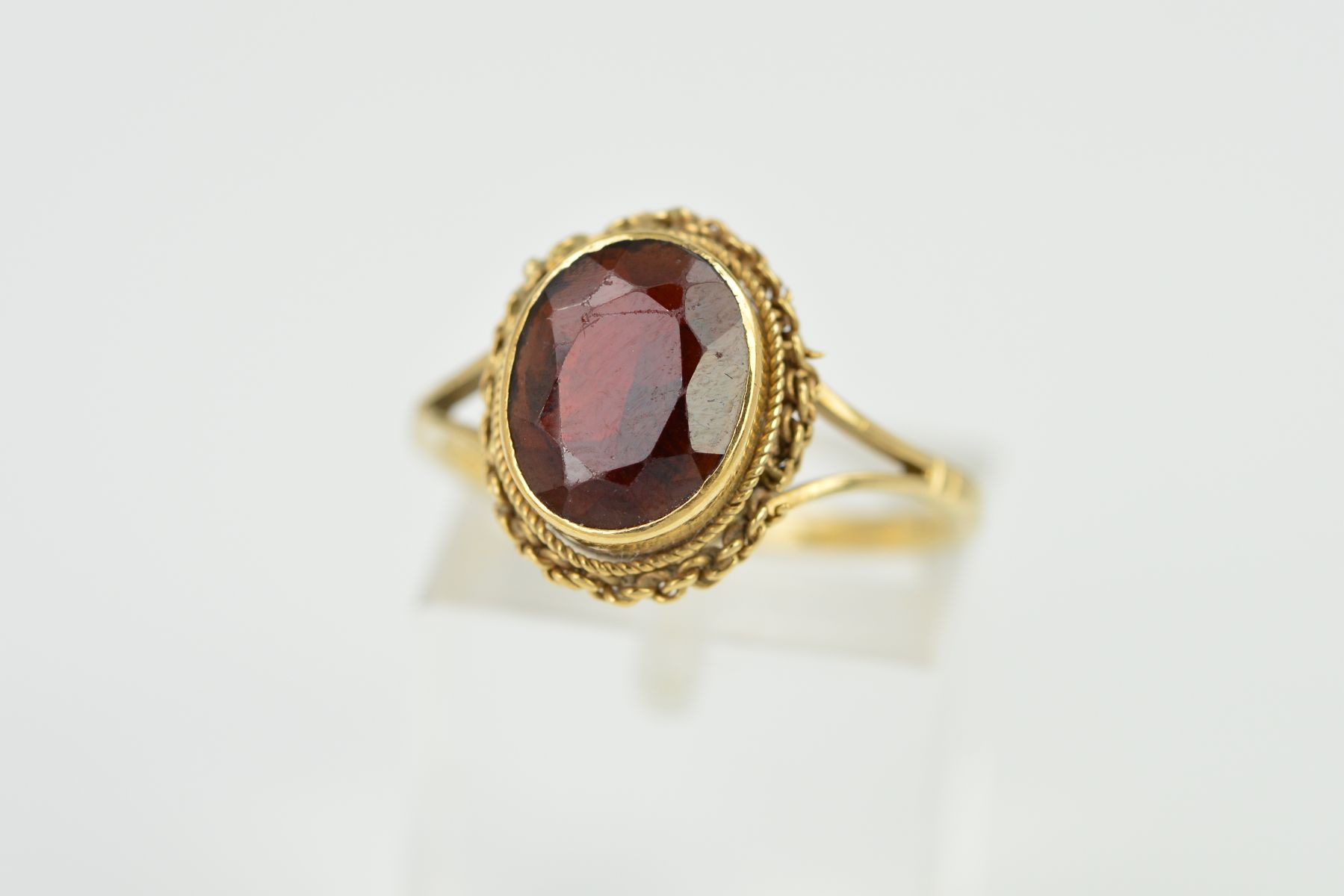 A 9CT GOLD GARNET RING, designed as an oval garnet within a collet setting within a rope twist and