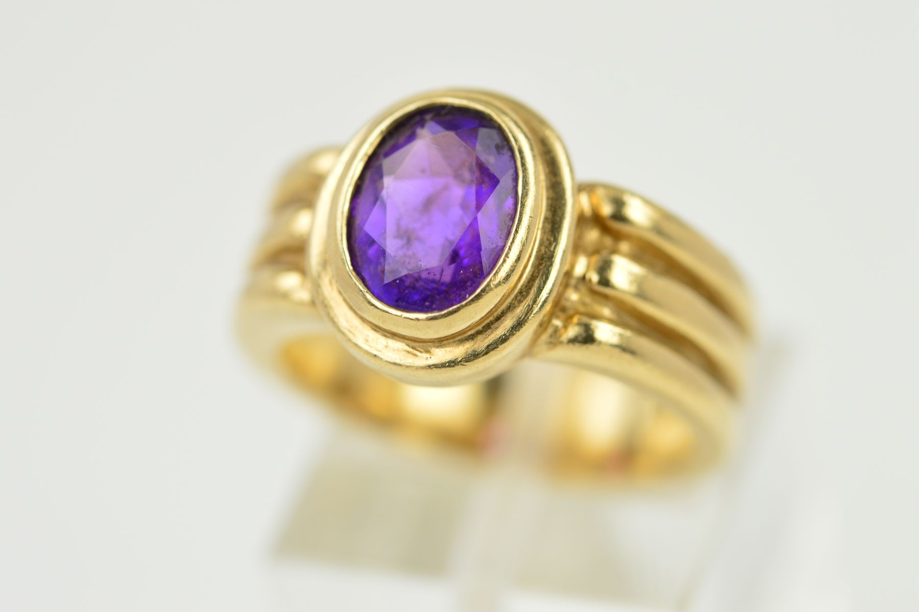 AN AMETHYST RING, the oval amethyst within a collet setting to the triple banded shank, stamped 9ct,