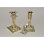 A PAIR OF LATE VICTORIAN/EDWARDIAN CANDLESTICKS, square sconces, reeded, cylindrical columns,