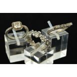THREE CUBIC ZIRCONIA DRESS RINGS to include a bow design and floral band, each stamped '925'